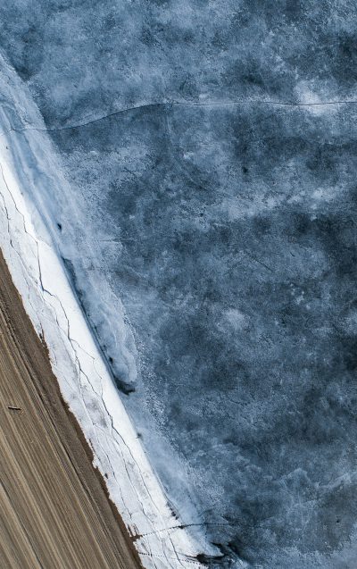 Aerial view of an ice field with wooden boards, a long line across the center is visible in blue gray tones. The photography has a minimalist, high resolution and high detail style. --ar 5:8