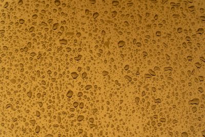 A top view of water droplets on the surface, creating an abstract pattern against a golden background. The texture is detailed and realistic with visible drops of raindrops. This wallpaper perfect for adding depth to your digital or print projects. --ar 128:85