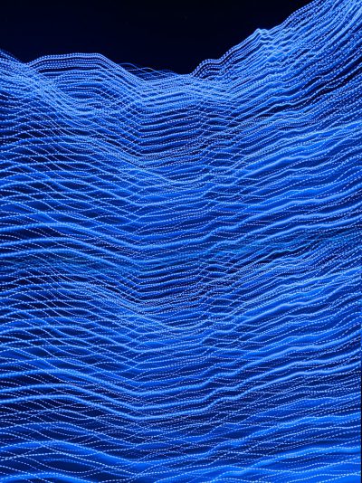 A blue wave of digital data, composed entirely of tiny dots and lines, creates the appearance of undulating ocean waves against a dark background. The scene is captured in high resolution with a macro lens, showcasing intricate details that give depth to each dot's shape and size. The focus is on the face. --ar 95:128