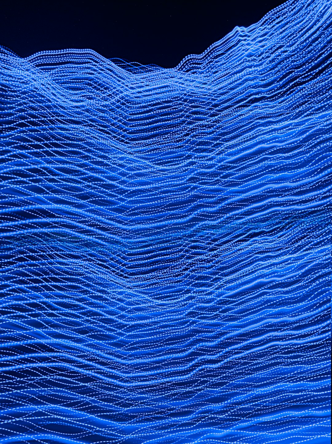 A blue wave of digital data, composed entirely of tiny dots and lines, creates the appearance of undulating ocean waves against a dark background. The scene is captured in high resolution with a macro lens, showcasing intricate details that give depth to each dot’s shape and size. The focus is on the face. –ar 95:128