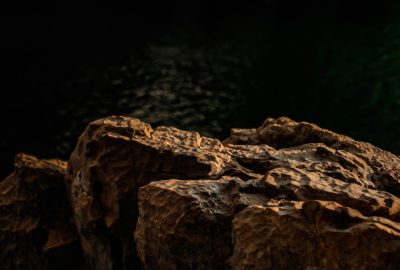 Closeup of rough textured rocks with a dark background and warm lighting, captured with a Sony A7R IV and f/2 lens from a low angle, with high detail focused on showcasing the texture contrast and depth. --ar 64:43