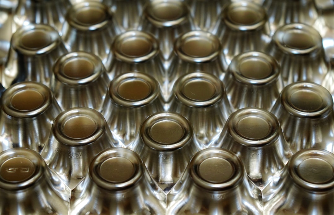 A closeup of the top view of empty glass bottles with metal caps arranged in repeating rows, showcasing their uniform appearance and texture. The bottles are arranged neatly on one side to create symmetry and emphasize their design details. This perspective highlights each bottle’s shape and pattern, emphasizing the beauty found within them. The neutral background allows for easy asset design or graphic creations using these bottle images in the style of graphic designers. –ar 64:41