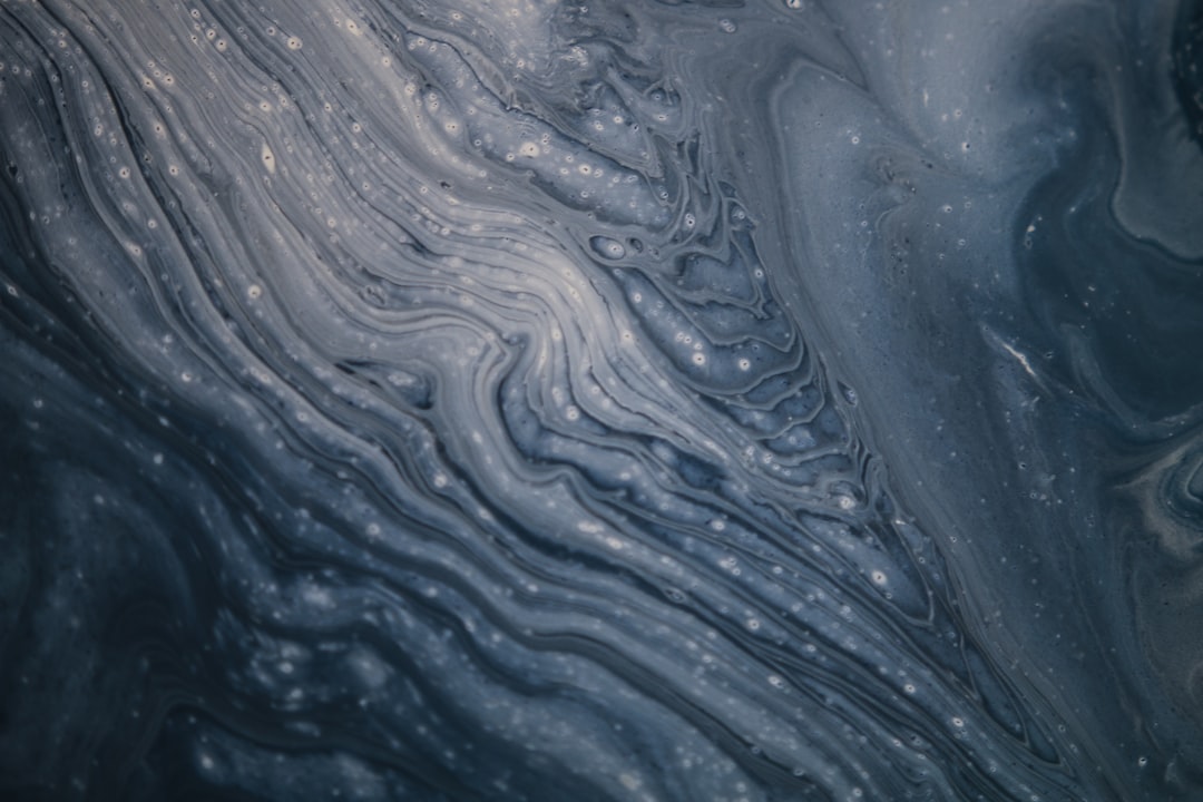 Abstract fluid art background with swirling liquid in dark blue and gray colors. The texture resembles the surface of an ocean or sea, with ripples creating intricate patterns reminiscent of water flow. There is a hint of bubbles on top to add depth and movement. This design would be suitable for creative backgrounds, covers, cards, posters, etc., –ar 128:85