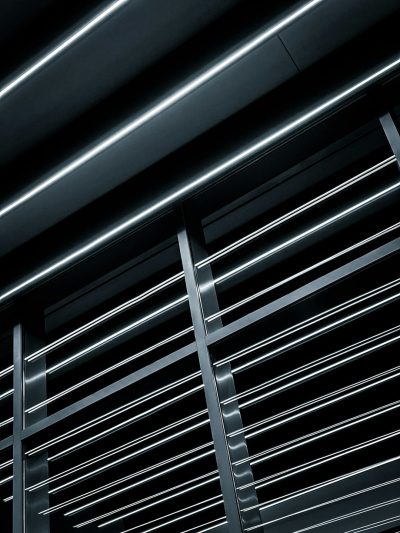 A closeup of the steel slats on an office ceiling, illuminated by soft LED lighting against a dark background. The details include thin lines and shadows that create depth in the composition. --ar 3:4