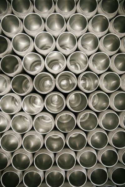 A symmetrical pattern of metal cups stacked on top of each other, arranged in neat rows and creating an abstract background. The metallic texture is visible through the open mouthed tubes, adding depth to the composition. --ar 85:128