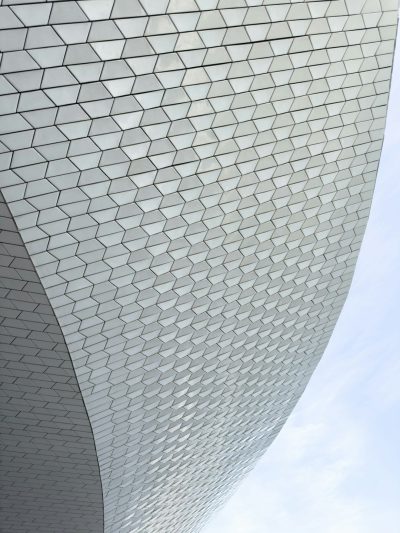 A closeup photo of the exterior wall texture, white and grey tiles in a hexagonal pattern with thin black lines on the edges, curved shape of the museum building against a light sky background, in the style of modern architecture, architectural photography, archdaily --ar 3:4