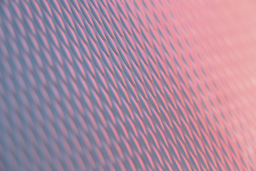 Closeup of the texture and pattern on an interior building wall, captured in pink and blue tones. The photograph highlights detailed lines that create visual interest. Soft lighting creates gentle shadows, adding depth to the composition. This image is perfect for use as background or wallpaper with copy space. It evokes tranquility and warmth, offering a serene atmosphere. The image can be used for design purposes in various settings such as home decor, in the style of a tranquil environment. –ar 128:85