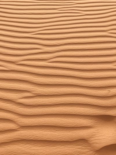 A closeup of the texture of sand dunes in the desert, featuring undulating lines and natural colors. The background is an endless sea of orange-brown earth. Natural light, low angle view, UHD, super detail in the style of natural light. --ar 3:4