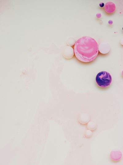 White background, pink and purple bubbles floating on the surface of white milk in the center of the picture, surrounded by some other colors of paint, scattered around, flat view, minimalist style, delicate texture, light color tone, high saturation, macro lens, soft lighting, delicate details, and visual impact. --ar 3:4