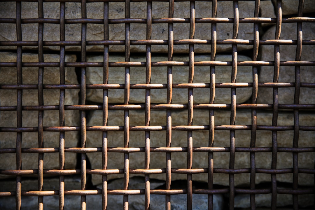 A closeup of the woven pattern on an old, rusty iron screen, with each line and weave detailed in high resolution. The background is neutral to highlight the intricate details of the metalwork in the style of the artist. –ar 128:85