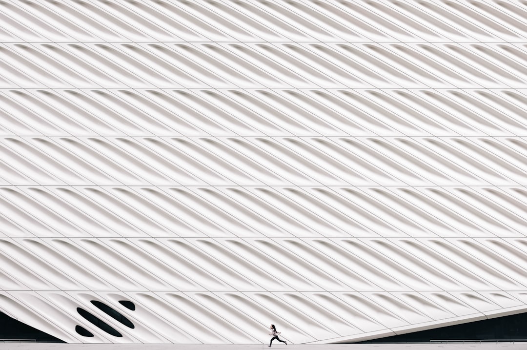 The Broad Museum, Los Angeles, has a white facade with patterned vertical lines. A close up photo shows a person running across the roof. The minimal architecture photography highlights architectural details in the style of the museum. –ar 128:85