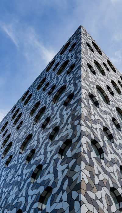 A tall building made of geometric patterned tiles, the facade is covered in black and white mosaic tiles with a blue sky background, architectural photography with realistic details in the style of ray tracing. --ar 73:128