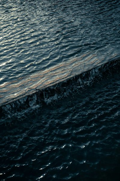 photograph of dark water surface with small waves, edge is made out of wood and metal, evening light, close up, aerial view --ar 85:128