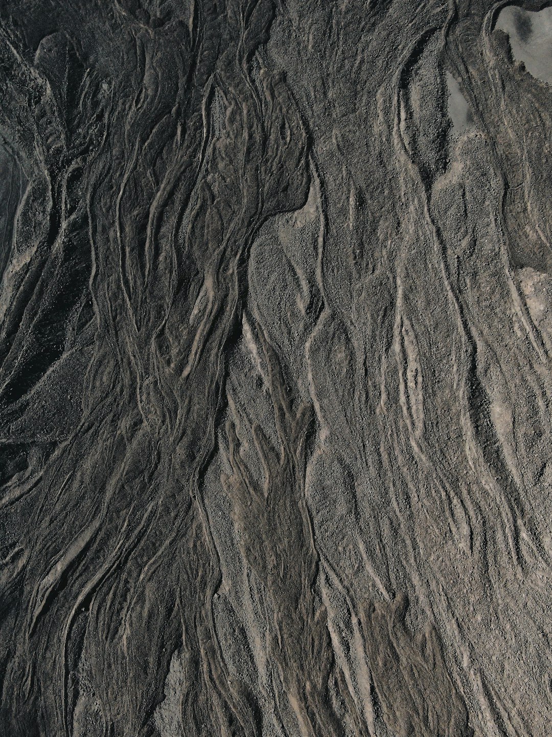 Aerial photography of the top view, closeup sand texture patterns on rocks and rivers, naturalistic landscape style, black and gray tones, dark background, wide angle lens, symmetrical composition, soft lighting, mysterious. High definition photography, high resolution. –ar 3:4