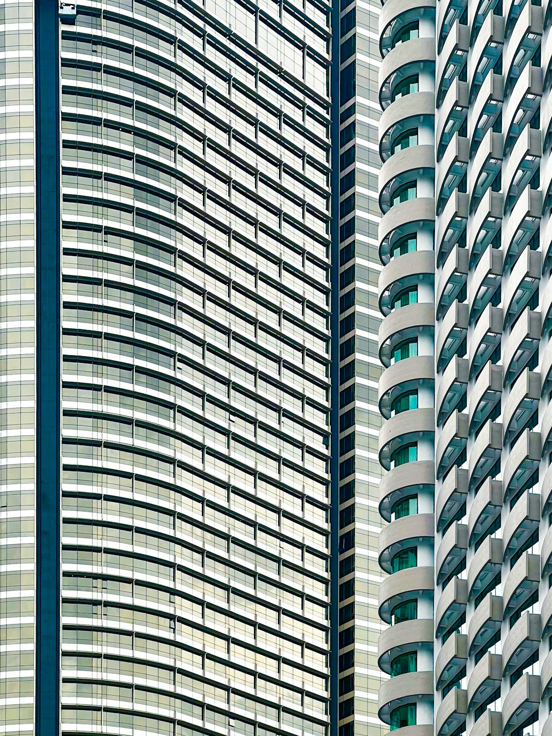 Closeup of the curved facades and balconies on two modern highrise buildings in Hong Kong. The building is made up of large glass windows with white vertical stripes that create an interesting pattern against the green background. This photo was taken during daylight to highlight details such as textures, shapes, colors, reflections, shadows, light rays, and highlights. It has been digitally altered in the style of an octane render. –ar 3:4