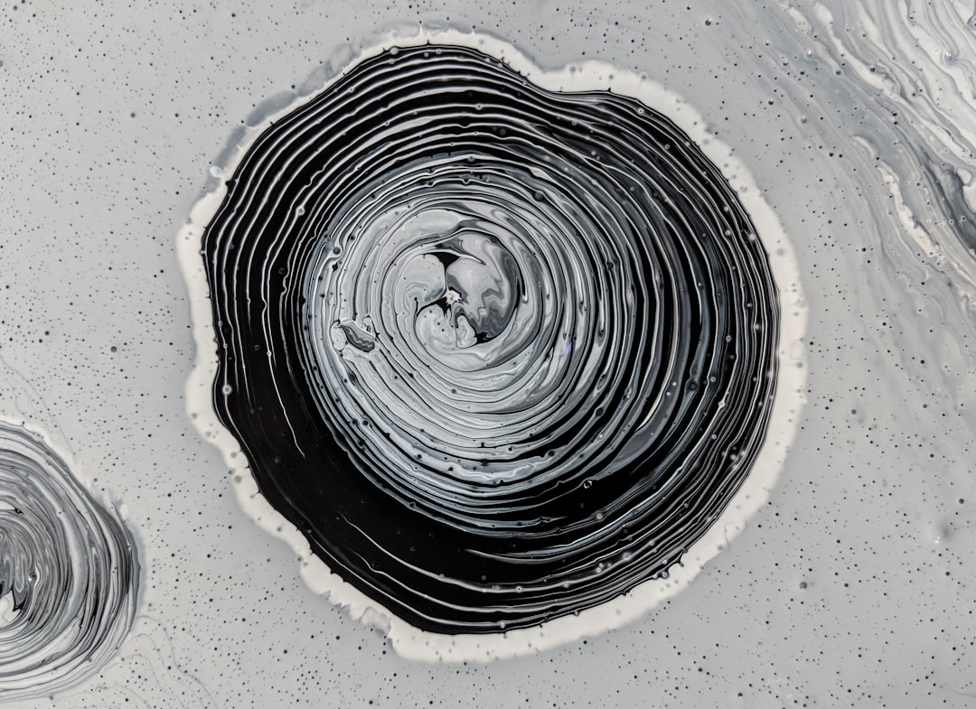 A black and white acrylic painting of circular swirls, paint splashes in the shape of an inkwell on top of it, on a grey background, in the style of a drone view. –ar 128:93