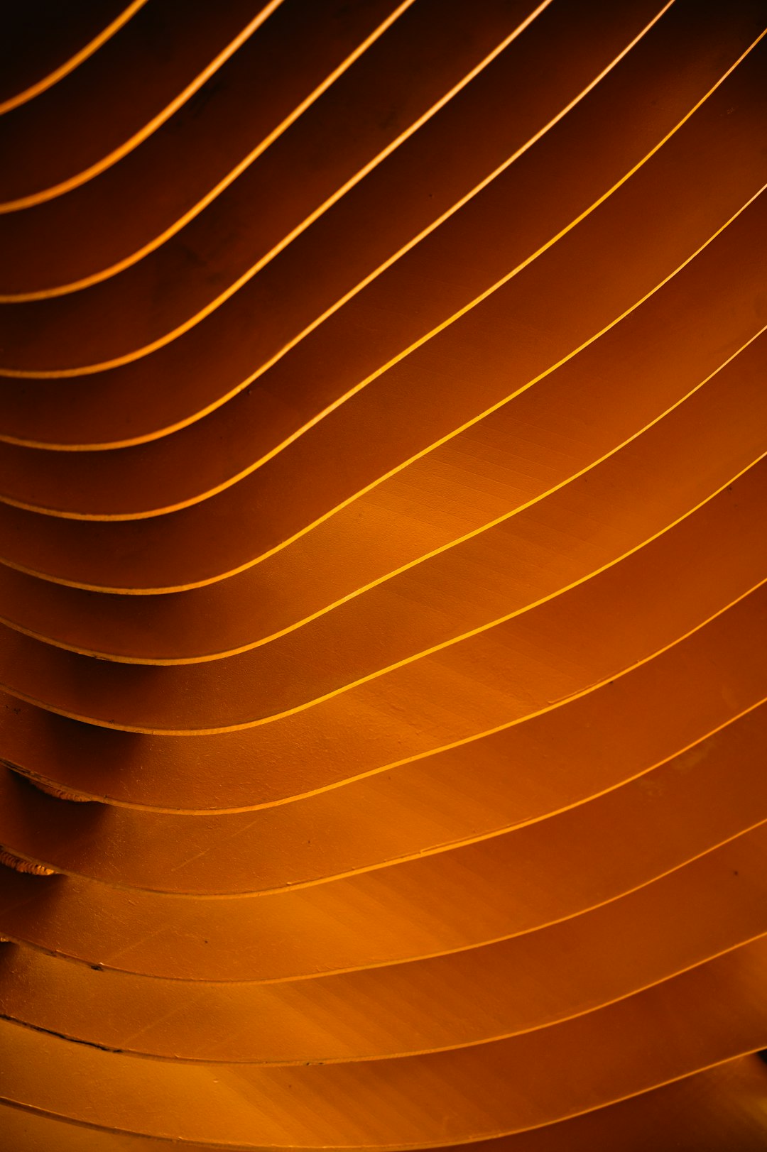 A closeup of the curved lines on an orange-colored wooden ceiling, creating a warm and inviting atmosphere with soft lighting. The wood has a natural grain texture that adds depth to the composition. This is perfect for a background or wallpaper design in the style of a natural wooden ceiling. –ar 85:128