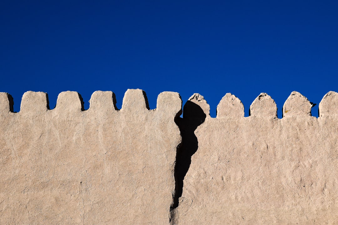 Photo of a wall with the shadow cast in the style of an ancient mud brick palisade in the desert against a blue sky, in a minimalist style, award winning photography –ar 128:85