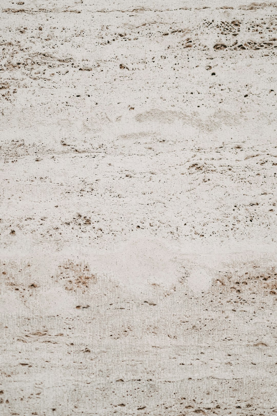 A closeup of the texture of travertine, a light grey and brown color with visible small holes and tiny cracks. The background is plain white to highlight its unique patterned surface. This top view image captures the natural beauty of the stone material. –ar 85:128