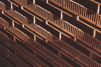 Aerial view of an office building balcony with wooden railings, captured from above in a closeup shot. The composition focuses on the symmetry and order within rows of brown wood balustrades, creating a sense of depth and structure. Soft lighting casts gentle shadows across each railing, adding to its architectural charm. This image captures both texture and form, showcasing how these iron guardrail accents enhance the aesthetic appeal of urban architecture. --ar 128:85