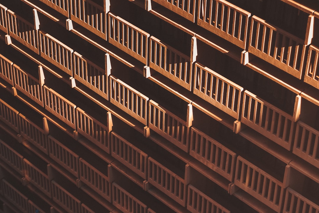 Aerial view of an office building balcony with wooden railings, captured from above in a closeup shot. The composition focuses on the symmetry and order within rows of brown wood balustrades, creating a sense of depth and structure. Soft lighting casts gentle shadows across each railing, adding to its architectural charm. This image captures both texture and form, showcasing how these iron guardrail accents enhance the aesthetic appeal of urban architecture. –ar 128:85