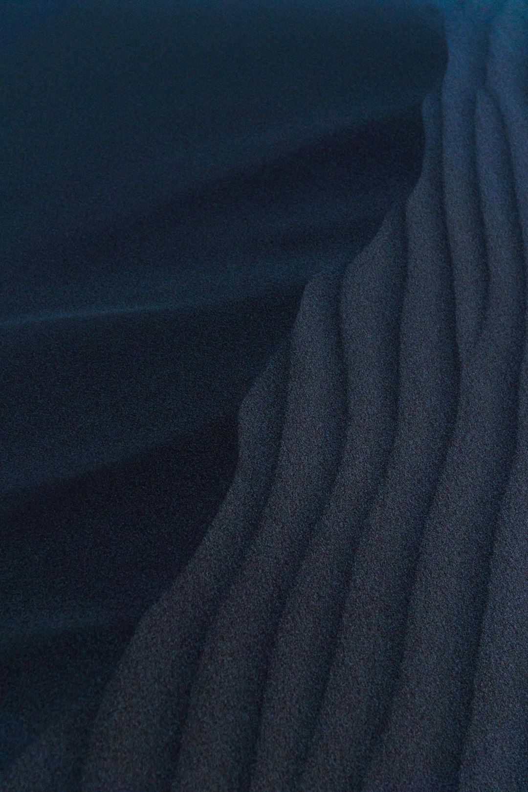 Close up of dark sand ripples, dark blue sky, nighttime at the desert dunes, minimalist and cinematic. The scene depicts desert dunes at nighttime under a dark blue sky with close up view of dark sand ripples, rendered in a minimalist and cinematic style. –ar 85:128