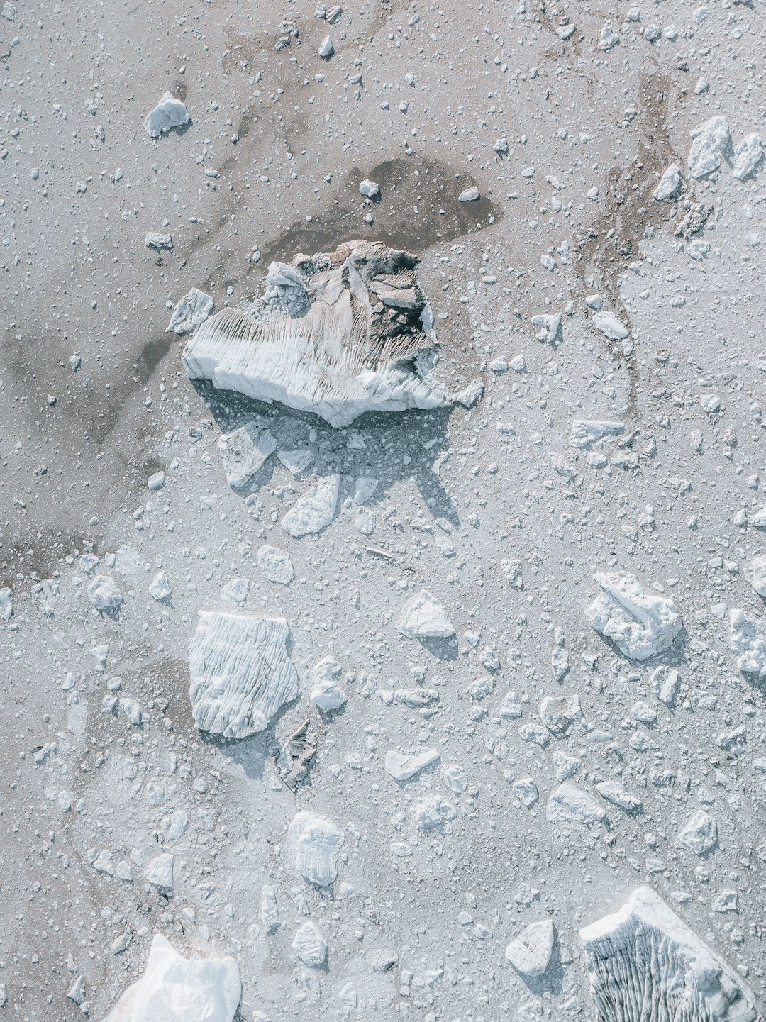 flat lay top view of the antarctic ice shelf with small rocks and debris scattered around, no snow on ground, no people or animals visible, drone shot, overhead view, white color palette, natural lighting, hyper realistic –ar 95:128