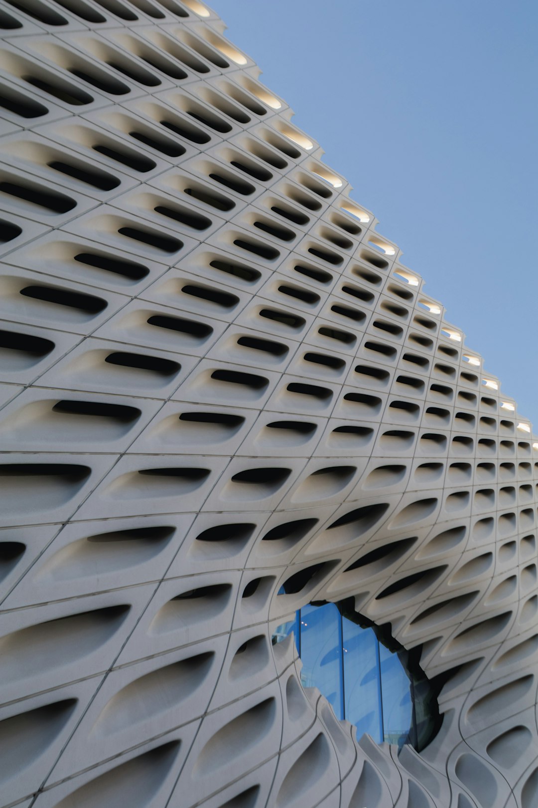 The Broad Museum in Los Angeles, designed in the style of Heatherwick Studio, has a facade with a parametric lace pattern and slanted windows. A close up shot shows the texture of the building against a blue sky background in architectural photography for Archdaily architecture. –ar 85:128