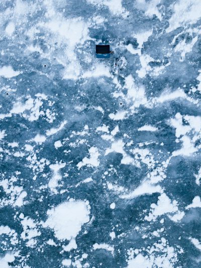 Aerial view of ice on lake with small black square object floating in middle, blue and white colors, ultra realistic photography --ar 95:128