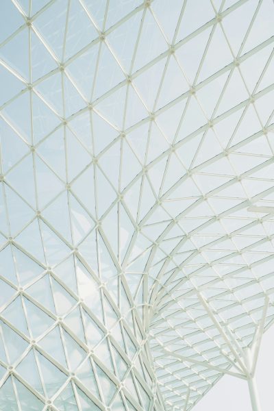 A closeup photo of the roof structure, composed of white metal frames and glass panels, is located in an open space with clear sky. The frame forms triangular shapes that create geometric patterns on top. This modern architectural design creates a unique visual effect against light blue tones. High resolution photography, natural lighting, soft shadows, and minimalist composition.,,in --ar 85:128