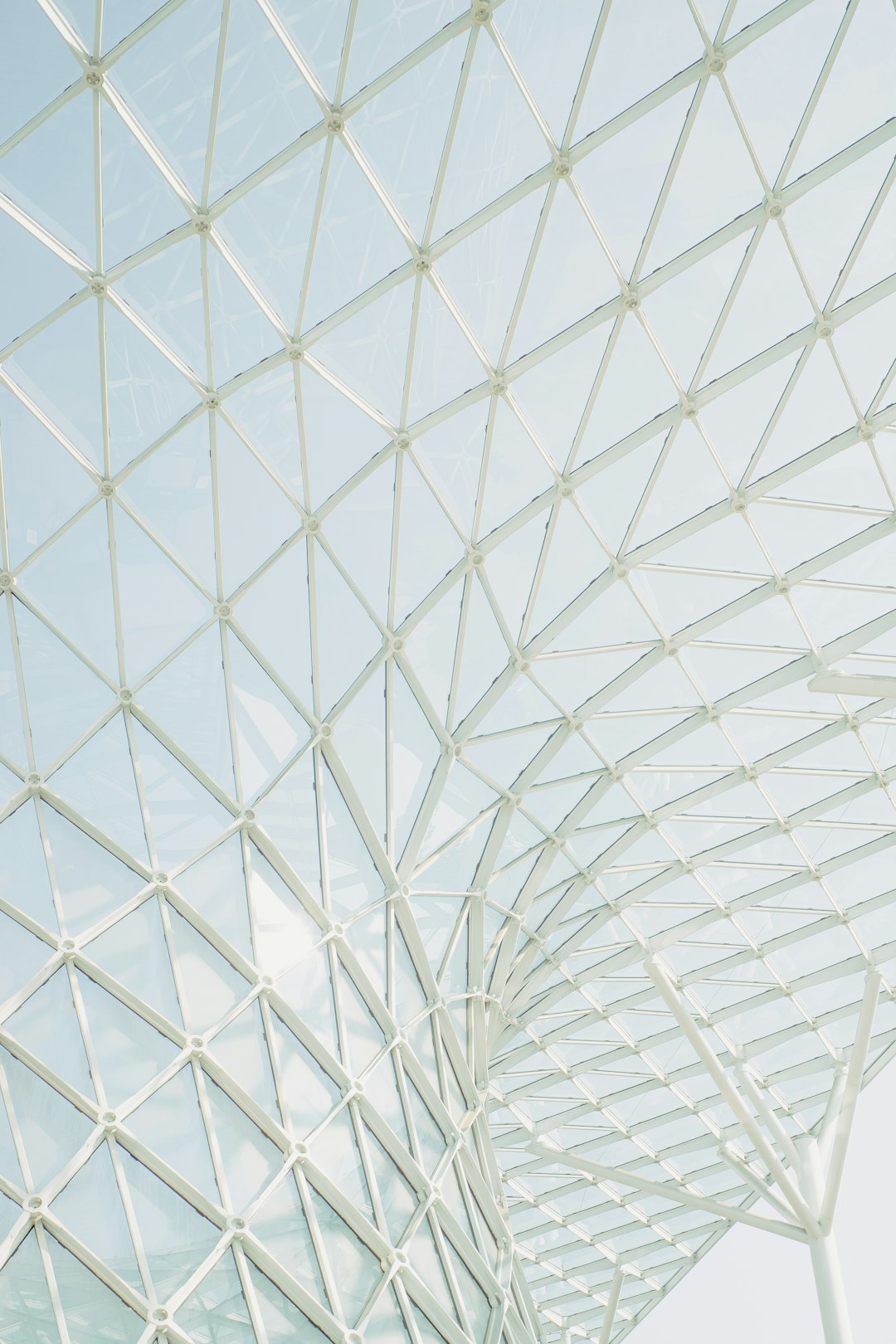 A closeup photo of the roof structure, composed of white metal frames and glass panels, is located in an open space with clear sky. The frame forms triangular shapes that create geometric patterns on top. This modern architectural design creates a unique visual effect against light blue tones. High resolution photography, natural lighting, soft shadows, and minimalist composition.,,in –ar 85:128