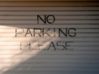 A photo of the text "NO parking please" written on a white garage door in daylight with shadows. --ar 4:3