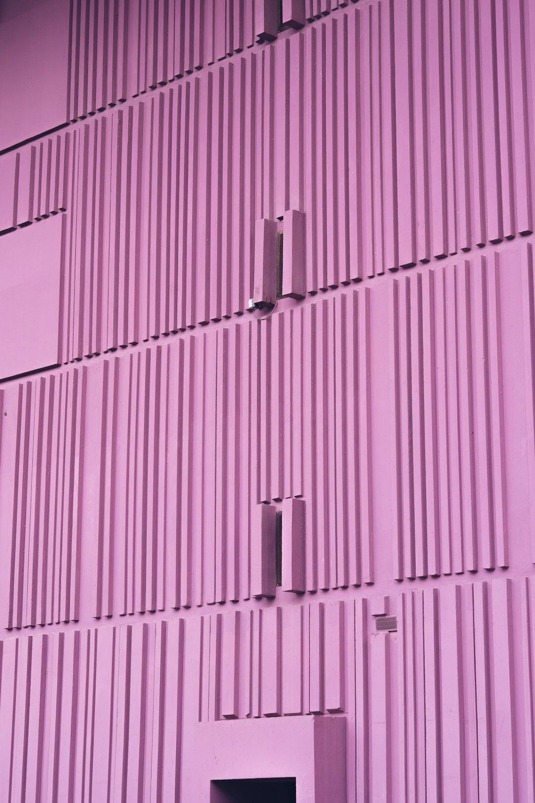 Pink metal wall with vertical lines, front view, pink purple color scheme, simple background, building facade photography, front closeup, symmetrical composition, bright light, minimalism, architectural details, architectural appearance, and sense of space. The building is made up of many small squares, which gives it an extremely interesting shape. This photo was taken by Sony Alpha A7 III camera. –ar 85:128