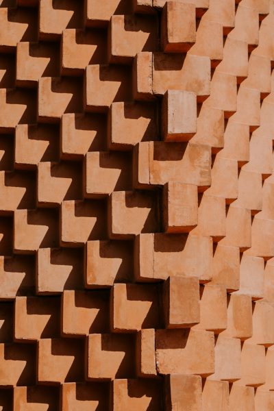 A terracotta wall made of interlocking blocks, each block shaped like an E Upward angle shot, with the focus on intricate geometric patterns and natural lighting. --ar 85:128