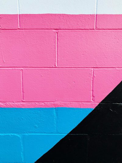 Black, pink and blue wall with a large black triangle painted on it. The colors of the flag are white, pink and dark blue. A closeup photo of part of an urban brick mural. Minimalist aesthetic. In the style of an urban mural, a closeup photo of bricks features a pink, blue and black geometric shape. The colors are white, hot pink and dark blue. --ar 3:4