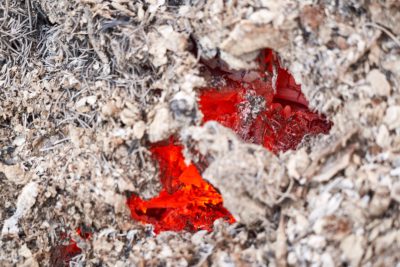 Closeup of a red plastic burned piece in dry gray soil, photographed from above in natural light with global illumination and white balance, taken with a Canon EOS R5 in the style of natural light. --ar 128:85