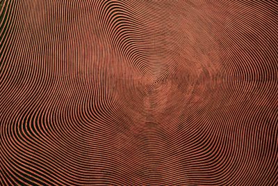 A photograph of an intricate pattern made from red lines on copper, creating the illusion that they form circular shapes in front and back view. The background is solid black to highlight the detailed texture of each line, creating a visually captivating effect. --ar 128:85