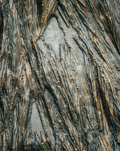 A closeup of the texture on an old tree trunk, with dark gray and brown hues creating intricate patterns that resemble liquid metal. The background is blurred to emphasize details. --ar 51:64