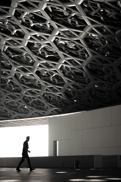 Abu Dhabi Victoria Street, modern museum interior made of a black and white parametric grid structure. The building is completely covered with a thin steel mesh that creates geometric patterns in the form of hexagons on all walls and ceiling. A person walking through the room, in the style of Rory Gardiner, with natural light, in a cinematic style. --ar 85:128