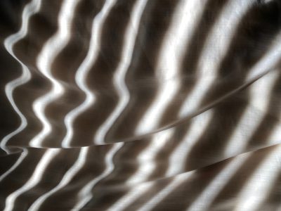 An abstract photograph of a patterned wave on the surface of fabric, soft light, shadows and highlights, neutral colors, close up. The photograph is in the style of a close up abstract image with soft light and shadows highlighting a patterned wave on the surface of fabric in neutral colors. --ar 4:3