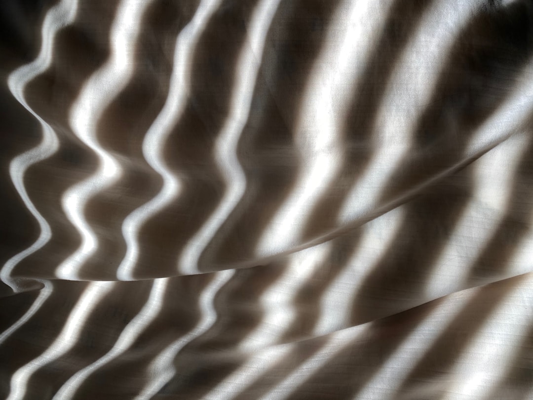 An abstract photograph of a patterned wave on the surface of fabric, soft light, shadows and highlights, neutral colors, close up. The photograph is in the style of a close up abstract image with soft light and shadows highlighting a patterned wave on the surface of fabric in neutral colors. –ar 4:3