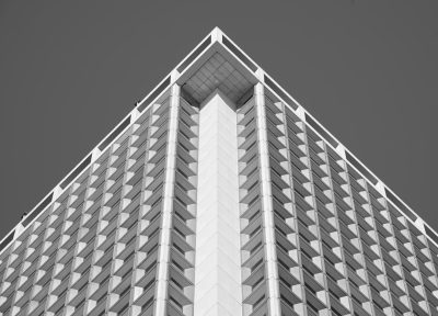 A tall building with a triangular shape, simple architecture, black and white photography in the style of symmetrical composition, high-angle shot, architectural details, modern design, geometric lines, urban setting. --ar 32:23