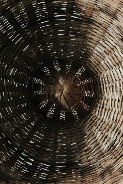 A close up of the inside of an old woven basket, with a spiral pattern. The photo was taken from above in a cinematic style, with a bokeh effect and depth blur over and under. Dark brown tones were used, with hyper realistic photography in the style of the subject. --ar 85:128