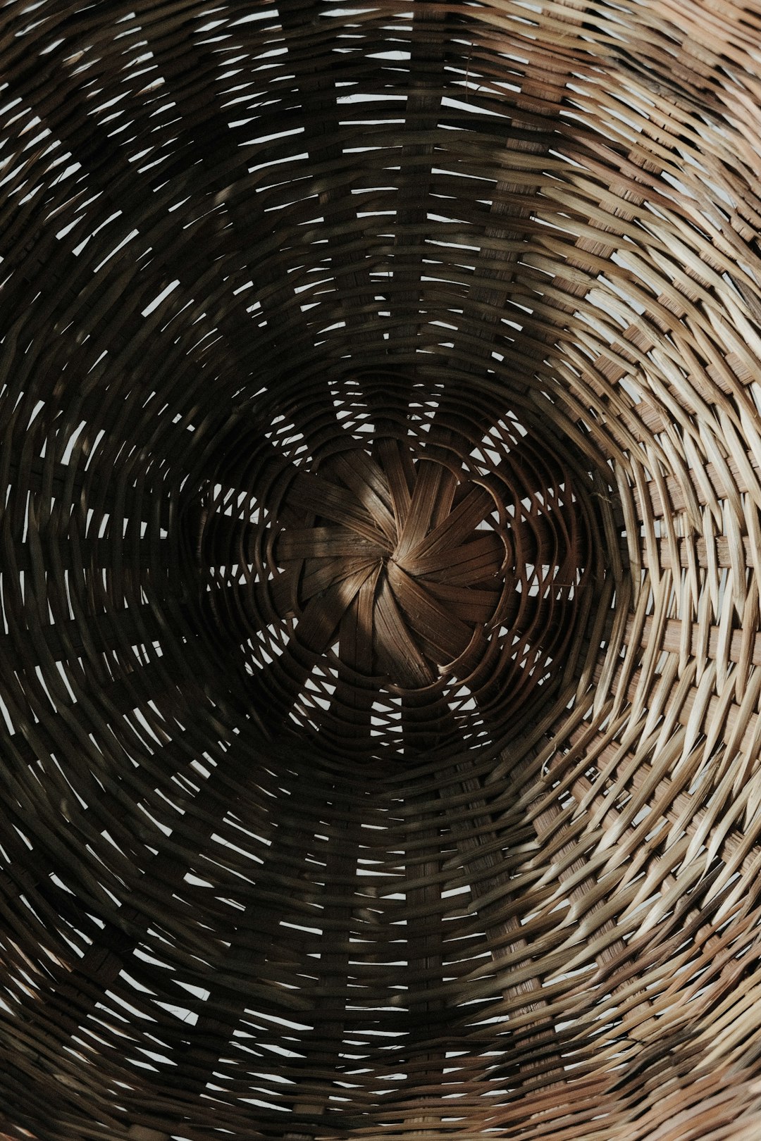 A close up of the inside of an old woven basket, with a spiral pattern. The photo was taken from above in a cinematic style, with a bokeh effect and depth blur over and under. Dark brown tones were used, with hyper realistic photography in the style of the subject. –ar 85:128