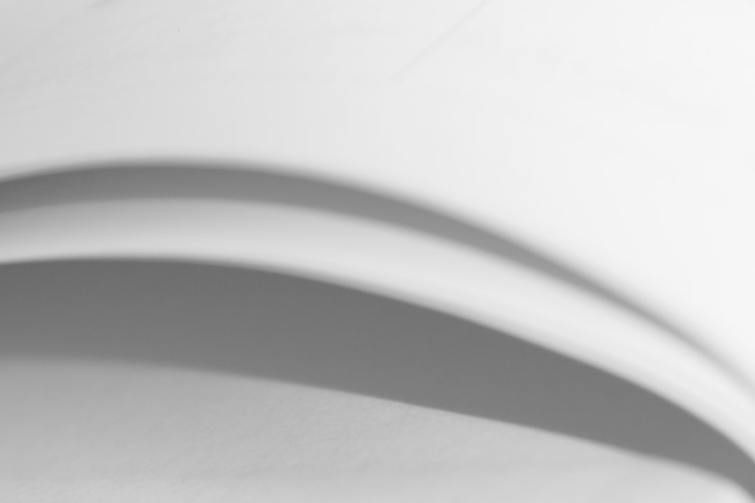 A closeup of the curved shadow on white paper, with a blurred background and high contrast between light gray and black, creating an abstract composition. The shadows cast by two slightly overlapping curves form a circular pattern on the surface of smooth paper, adding depth to the scene. This is a minimalist style that highlights the texture and shape of the shadow, giving it a modern feel. It’s suitable for use as a background or design element in various creative projects.,,in –ar 128:85