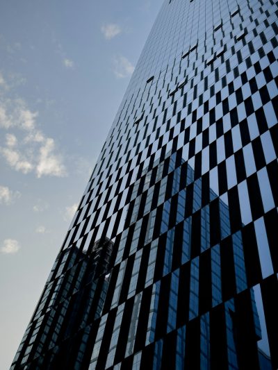 A tall building made of black glass, with geometric grid patterns on the side, a blue sky with white clouds in the background, taken from a low angle shot, with macro photography, architectural photography, at a high resolution, in a cinematic style, with volumetric lighting, in the hyper realistic style, with hyper detailed quality, rendered with octane render. --ar 3:4