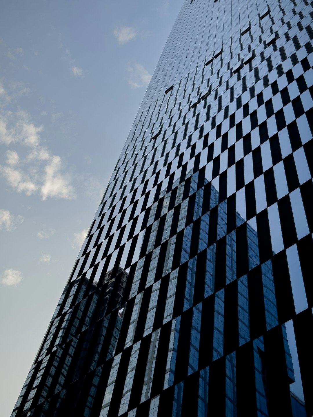 A tall building made of black glass, with geometric grid patterns on the side, a blue sky with white clouds in the background, taken from a low angle shot, with macro photography, architectural photography, at a high resolution, in a cinematic style, with volumetric lighting, in the hyper realistic style, with hyper detailed quality, rendered with octane render. –ar 3:4