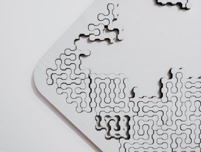 A close up of an empty white puzzle on the table, with geometric patterns, made from laser cut basswood and metal, product photography, on a blank background, in the style of nendo. --ar 128:97