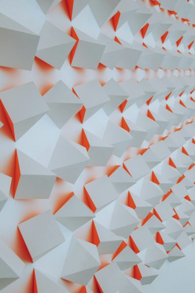 A wall of white and orange paper triangles, shown in close up, features geometric shapes arranged symmetrically in an art installation. The geometric shapes are arranged in the style of symmetrical art. --ar 85:128