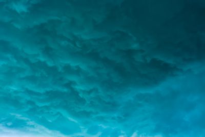 Abstract background of blue and teal storm clouds. The open sky has a textured, natural quality evoking weather. An aerial view of a dark, stormy sky with abstract cloud formations in various shades of blue, cyan and turquoise. --ar 128:85